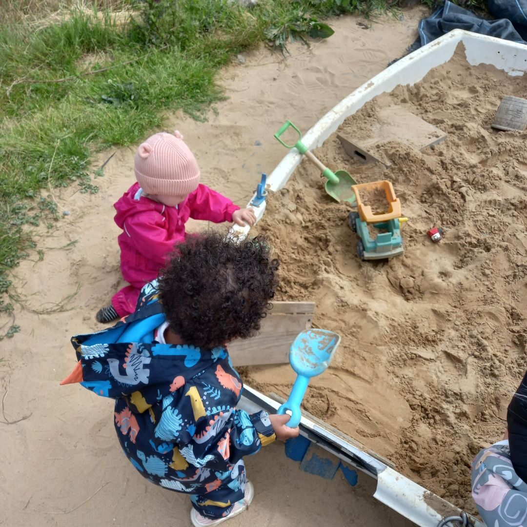A child playing in the sand pit with a water channel